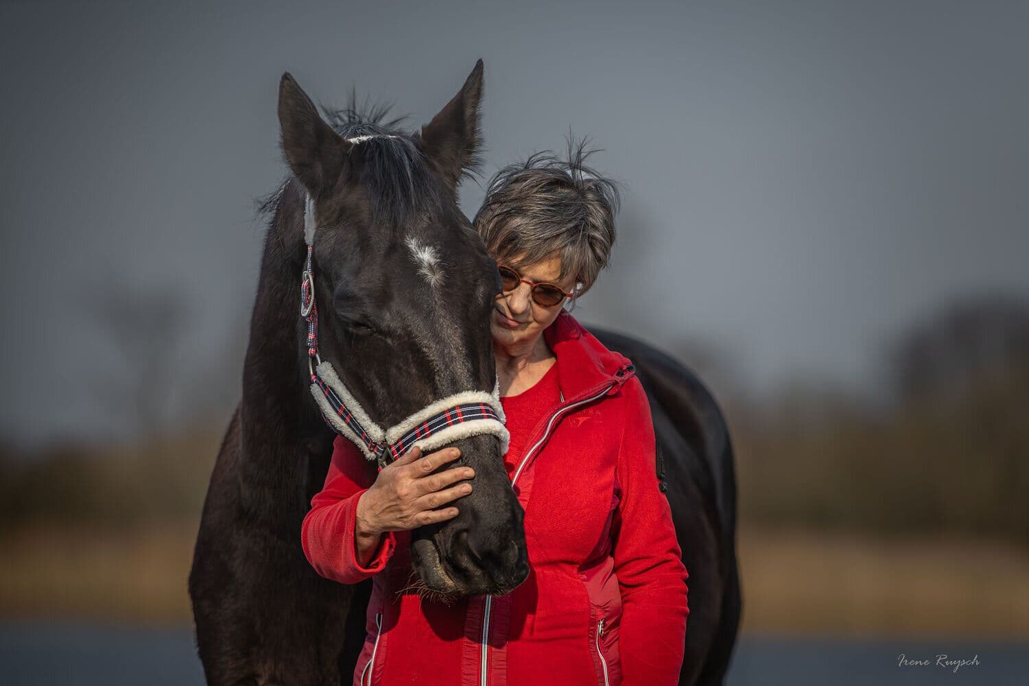 Mieke staat met haar hoofd tegen het hoofd van een donker paard